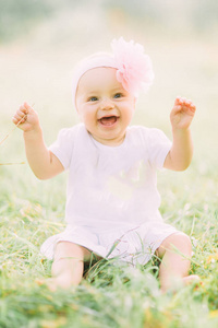 绿色草地背景下穿着白色连衣裙的快乐快乐孩子的肖像。公园里快乐的小宝贝。家庭概念
