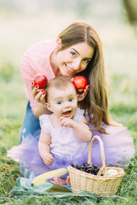 快乐的母子宝贝女孩在盛开的春天花园里玩水果。 母亲节假期概念