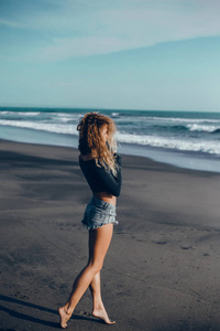 年轻漂亮的女孩在海滩上摆姿势，海浪，明亮的阳光和晒黑的皮肤