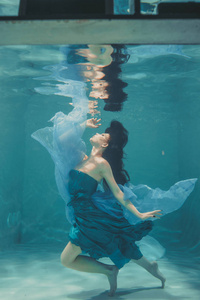 美丽的模特女孩穿着蓝色衣服在水下游泳，享受放松和缺乏压力