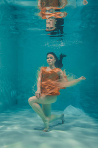 美丽的模特女孩穿着橙色衣服在水下游泳，享受放松和缺乏压力