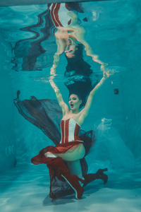 美丽的女孩在水下游泳运动风格，红色和白色恋物癖紧身胸衣和膝盖以上大腿高跟鞋与高跟鞋