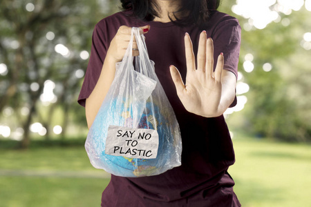 照片中的年轻女子拿着一个地球仪在塑料袋中，同时显示手势停止。 在公园里