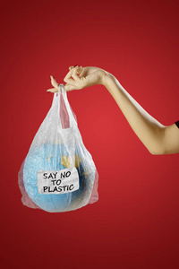 从塑料废物污染中拯救地球的概念。 年轻女子手里拿着一个地球仪，装在塑料袋里，上面写着拒绝的字样