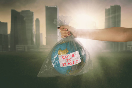 在现代城市背景下，年轻女子在塑料袋里拿着一个地球仪，上面写着对塑料的拒绝