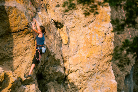 女孩爬上岩石。 登山者正在训练攀登岩石。 一个强壮的运动员克服了一条艰难的攀登路线。 极端的爱好。 一个女人在大自然中参加运动。