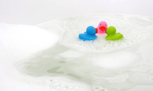 粉红色绿色和蓝色的鸭子在浴缸里被肥皂包围着