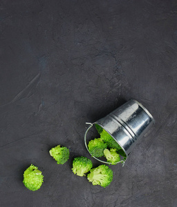 安抚绿色西兰花段从一个小桶。 黑暗背景下的健康饮食模式。 复制空间顶部视图。 素食。
