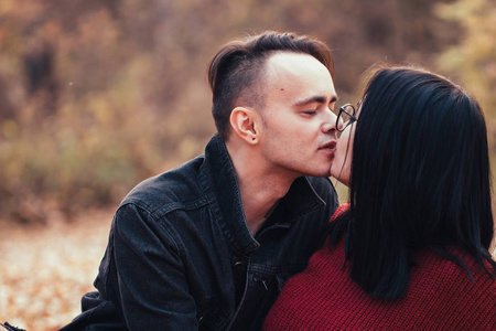 年轻的男人和年轻的女人坐在秋天森林里的格子上。