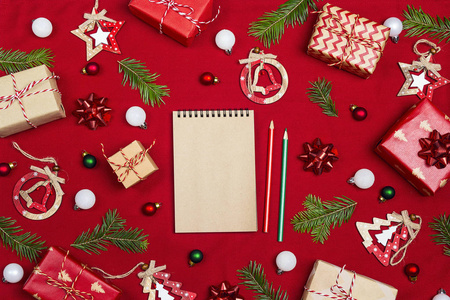 空白笔记本与圣诞节组成的礼物和装饰在红色织物背景。 放置一个愿望清单礼物或年度目标。 平躺式顶部视图