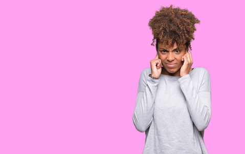 美丽的年轻非洲裔美国妇女，在孤立的背景上，用手指覆盖着耳朵，对响亮的音乐的噪音表达出恼怒的表情。 聋的概念。