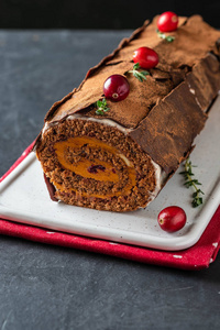 布什德诺伊尔。传统的圣诞甜点, 圣诞山核桃蛋糕与巧克力奶油, 红莓。在石头灰色背景与圣诞树分支