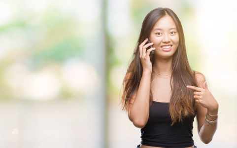 年轻的亚洲女人在电话中，在孤立的背景下说话，惊讶的脸指向自己