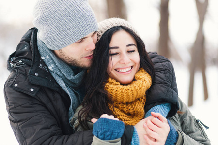 快乐的年轻夫妇享受寒假，微笑着拥抱在模糊的冬季景观背景上。
