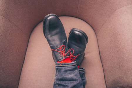 地把他的脚放在经典的皮鞋上,红色的鞋带和红色的时髦袜子放在椅子上