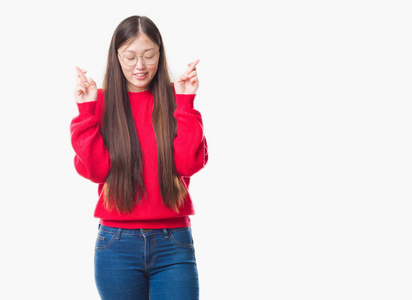 年轻的中国女人在孤立的背景上戴着眼镜，微笑着交叉手指，抱着希望，闭上眼睛。 运气和迷信的概念。