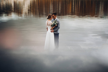 一对新娘在鞭子和新郎在灰色站立在湖之中