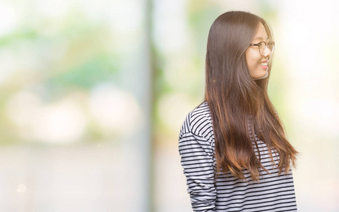 年轻的亚洲女人戴着眼镜，在孤立的背景上看着一边，脸上带着微笑，自然的表情。充满自信的笑。