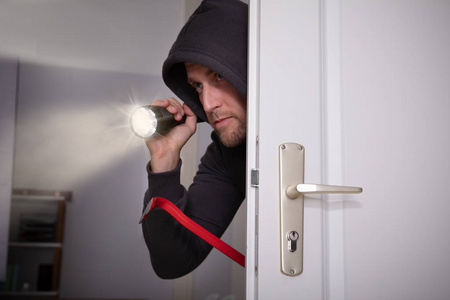 偷偷看小偷拿着手电筒和撬棍从门口偷看照片