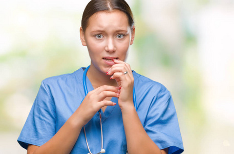 年轻的白种人医生女士穿着医疗制服，在孤立的背景下，看上去压力很大，紧张，双手咬着嘴的指甲。 焦虑问题。