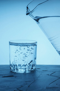 把水罐里的水倒进玻璃杯里。 饮用水从水壶里倒入蓝色背景上的玻璃杯里。