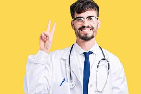 年轻的医生穿着医院外套，在孤立的背景上，用手指举着第二个，同时微笑着自信和快乐。