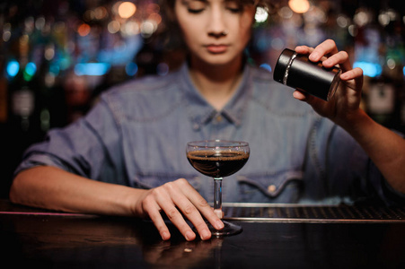 女性酒保在酒吧柜台上加入棕色酒精鸡尾酒中的粉末