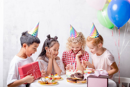 快乐的孩子们站在桌旁看着蛋糕的蜡烛