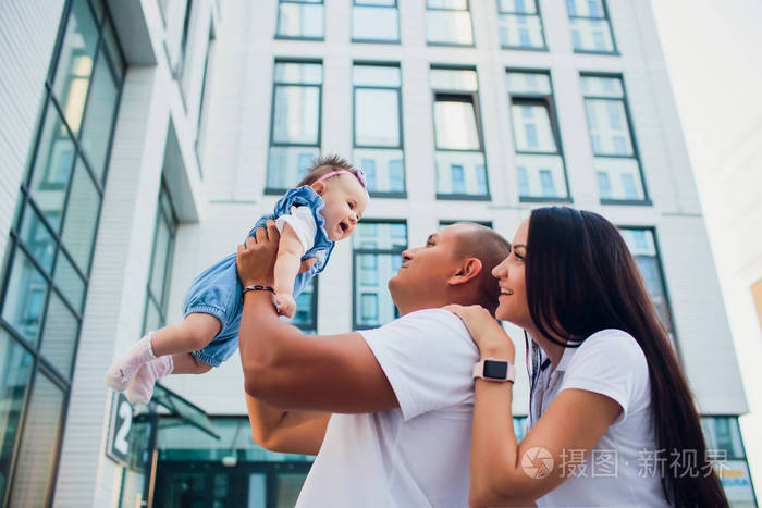 已婚夫妇, 抱孩子的人, 抱着男人的女人在他的肩膀上.在背景玻璃大厦
