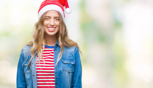 美丽的年轻金发女人戴着圣诞帽，在孤立的背景上，脸上带着快乐和凉爽的微笑。 幸运的人。