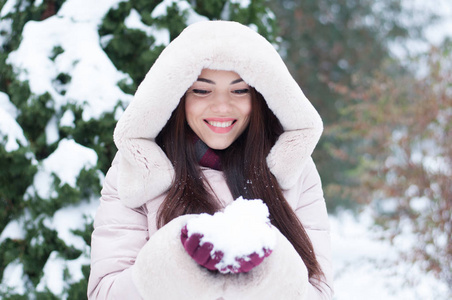 年轻美丽的情感女人的肖像，穿着带帽的羽绒服和手套，在白雪覆盖的花园背景上。 冬季雪景