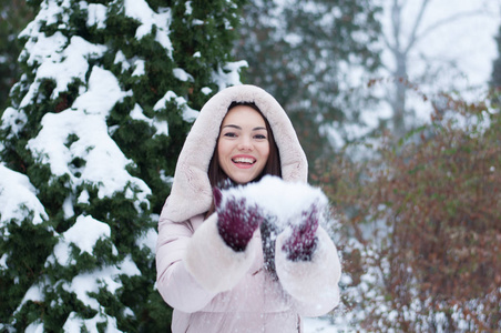 年轻美丽的情感女人的肖像，穿着带帽的羽绒服和手套，在白雪覆盖的花园背景上。 冬季雪景