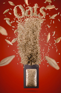 聚焦的燕麦种子从包装中飞出，在红色背景下冷冻在空气中。 演播室照片拍摄。 广告海报概念