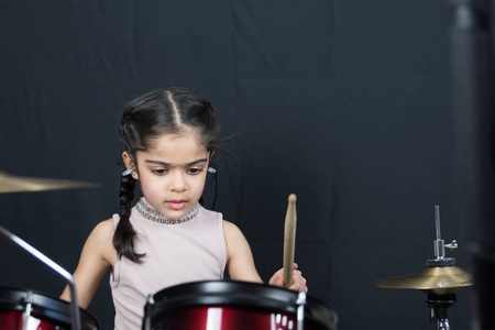一个5岁的英国印第安族女孩,在鼓上练习,在黑暗的黑色背景阅读音乐