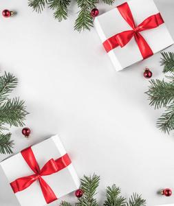 创意框架由圣诞杉枝在白纸背景上与红色装饰松果礼品盒。 圣诞节和新年主题。 平躺式顶部视图
