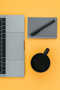 有彩色背景的工作场所。 笔记本电脑，一杯咖啡，一个记事本，一支笔隔在橙色的背景上。 平躺着