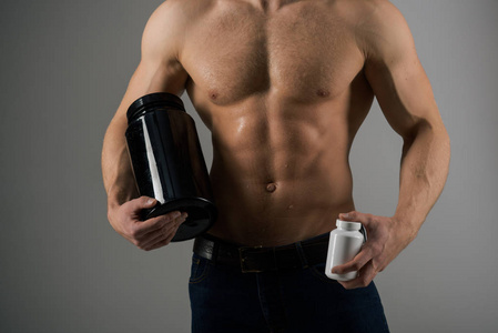 改变身体与饮食。合成代谢激素增加肌肉力量。强壮的男人拿着维生素瓶。有六包腹肌的人. 肌肉生长与合成代谢类固醇。维生素营养。健康饮