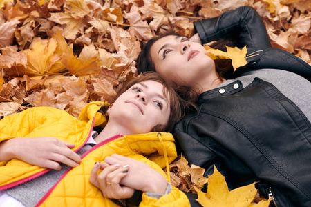 漂亮的女人和十几岁的女孩在秋天公园摆姿势。 他们躺在落叶上。 秋天的美丽景观。