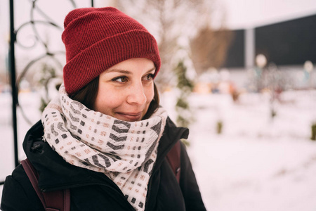 一个美丽的金发女郎戴着帽子和围巾在寒冷季节的城市景观背景上的肖像。 走在街上的女孩