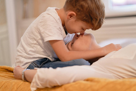 可爱的儿子和他可爱的妈妈正在抚摸他们的鼻子，一起躺在床上微笑