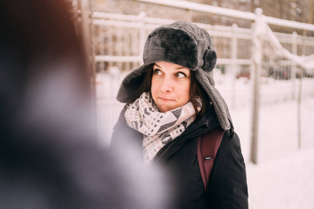 一个美丽的金发女郎戴着帽子和围巾在寒冷季节的城市景观背景上的肖像。 走在街上的女孩