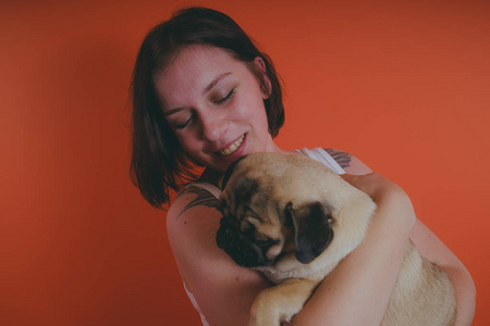 美丽的女孩纹身，手上拿着可爱的小狗在她的橙色背景。 人与狗之间友谊的概念。