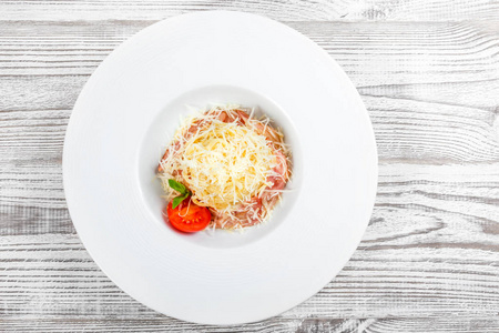 在清淡的木制背景意大利菜肴上，在盘子上放着肉火腿帕尔马干酪罗勒和番茄。 餐桌上的配料