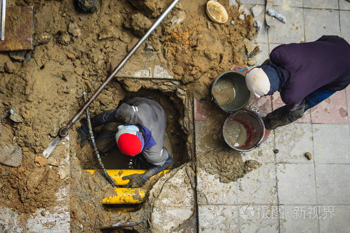 不明身份的水管工正在挖掘修理破裂的地下管道.