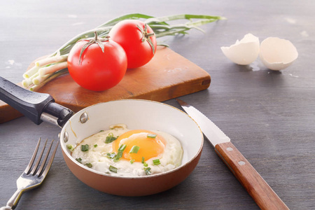 平底锅中的煎蛋西红柿和青葱是在木制的灰色桌子上做早餐的。