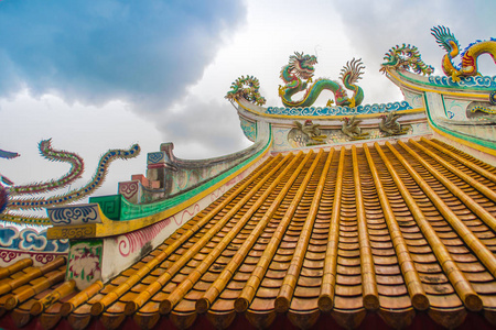 中国寺庙装饰瓷砖屋顶上爬行着美丽的大型鬼脸龙。 中国传统寺庙的彩色屋顶细节，蓝天背景上有龙像。 选择性聚焦。