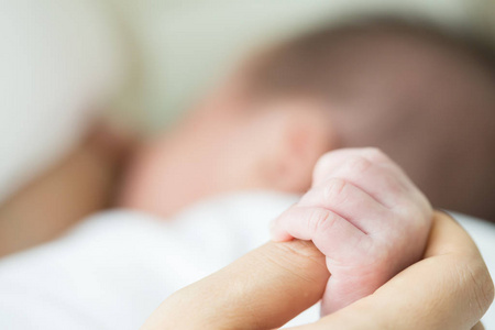 柔软的焦点和模糊的婴儿手触摸母亲的手，同时哺乳母亲