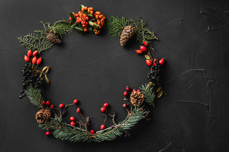 圣诞树的树冠，松果，浆果，坚果，黑色的石头背景。 圣诞节和新年快乐主题。 平躺式顶部视图