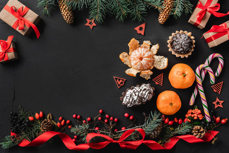 圣诞节组成的冷杉枝，松果浆果礼物和红色松弛的黑色石头背景。 糖果糖果，曼达林和许多礼物。 圣诞节和新年快乐主题。 平躺式顶部视图