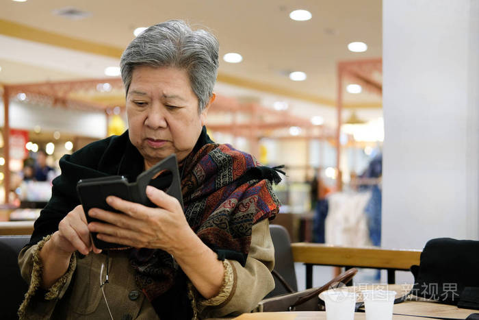 亚洲年长的女人在餐馆拿着手机老年人在咖啡馆使用智能手机老女人用